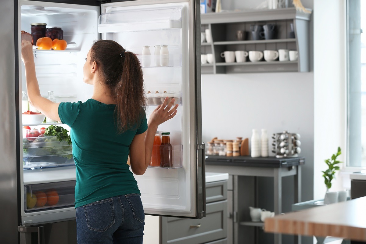 Người dùng mở cửa tủ lạnh nhiều ngăn đựng đầy thực phẩm trong căn bếp