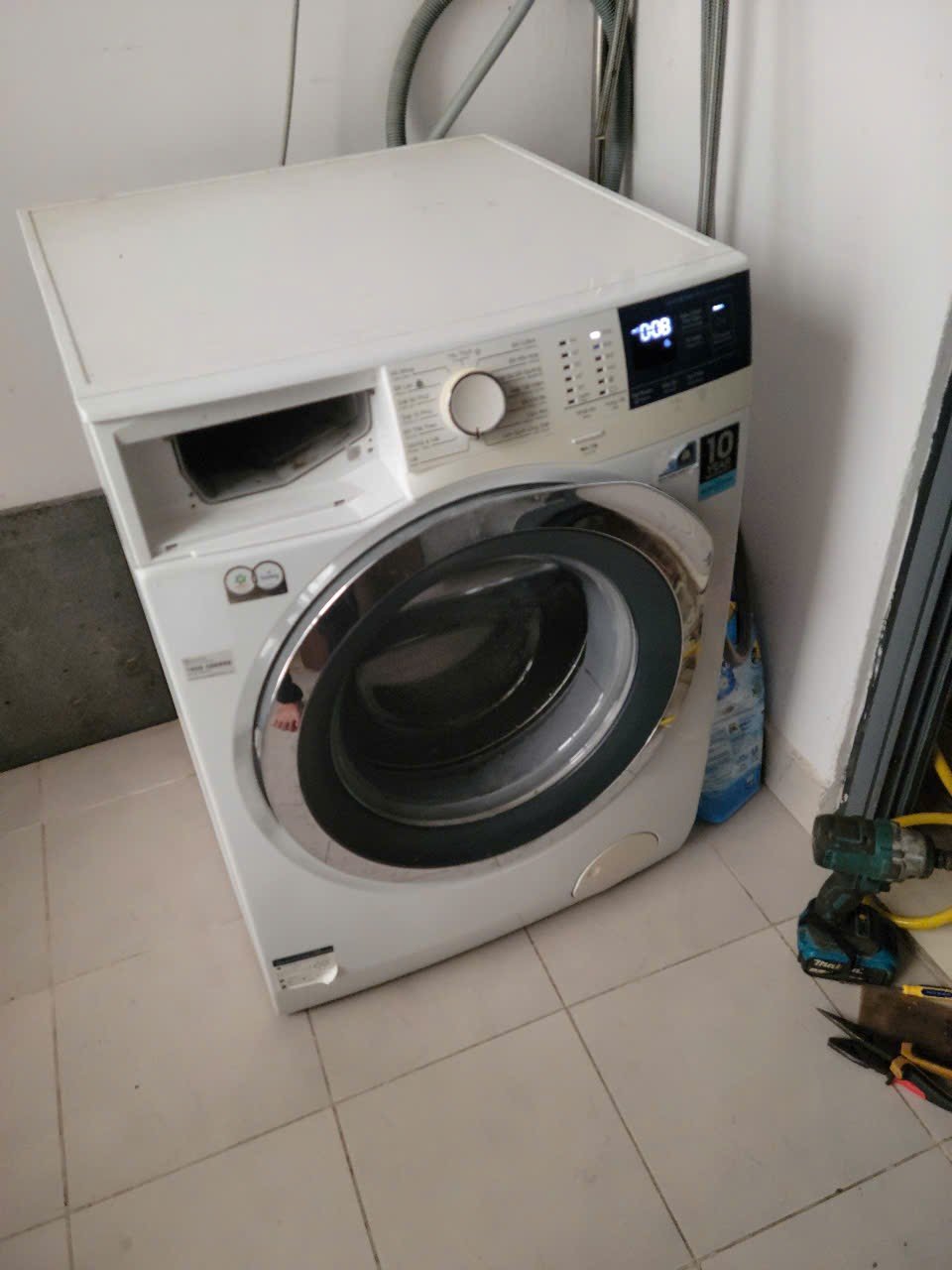 Máy Giặt Bị Trào Bọt: Nguyên Nhân Và Cách Xử Lý Ngay Máy giặt cửa ngang đặt trong nhà, ngăn đựng nước giặt đang mở, màn hình hiển thị thời gian còn lại