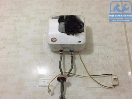 Bình nóng lạnh loại nhỏ gắn tường bị cháy đen toàn bộ mặt trước, dây dẫn và vòi sen vẫn còn nguyên bên dưới