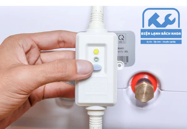 Bàn tay cầm cục chống giật ELCB gắn trên dây nguồn bình nóng lạnh, thấy rõ nút test màu vàng và đèn báo