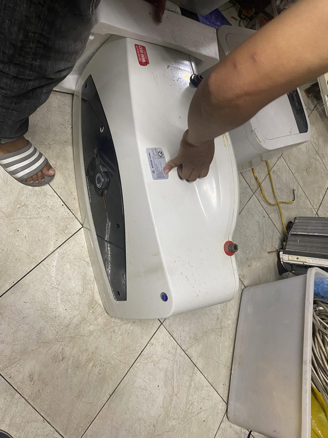 Thợ điện lạnh tháo vỏ bình nóng lạnh đặt dưới sàn để tiếp cận mặt bích